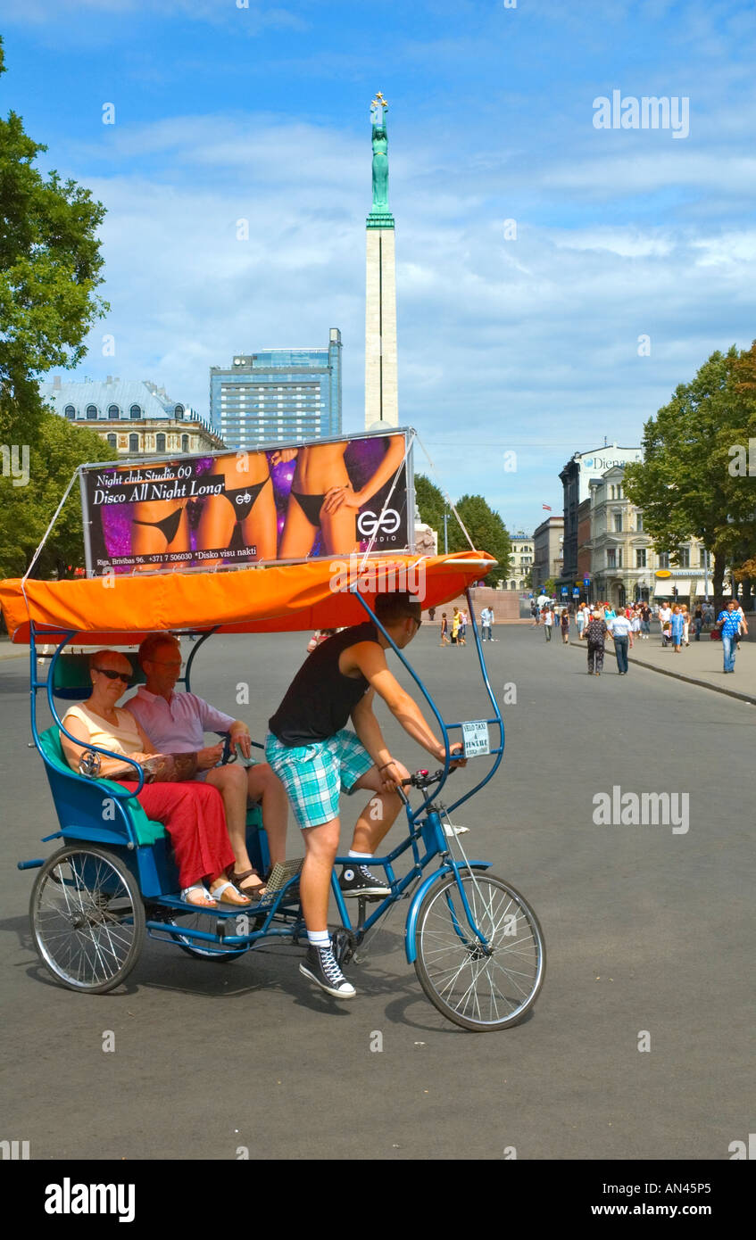 Un couple sur un velo chauffeur de taxi à l'avant du Monument de la liberté au centre de Riga capitale de la Lettonie en Europe du nord Banque D'Images