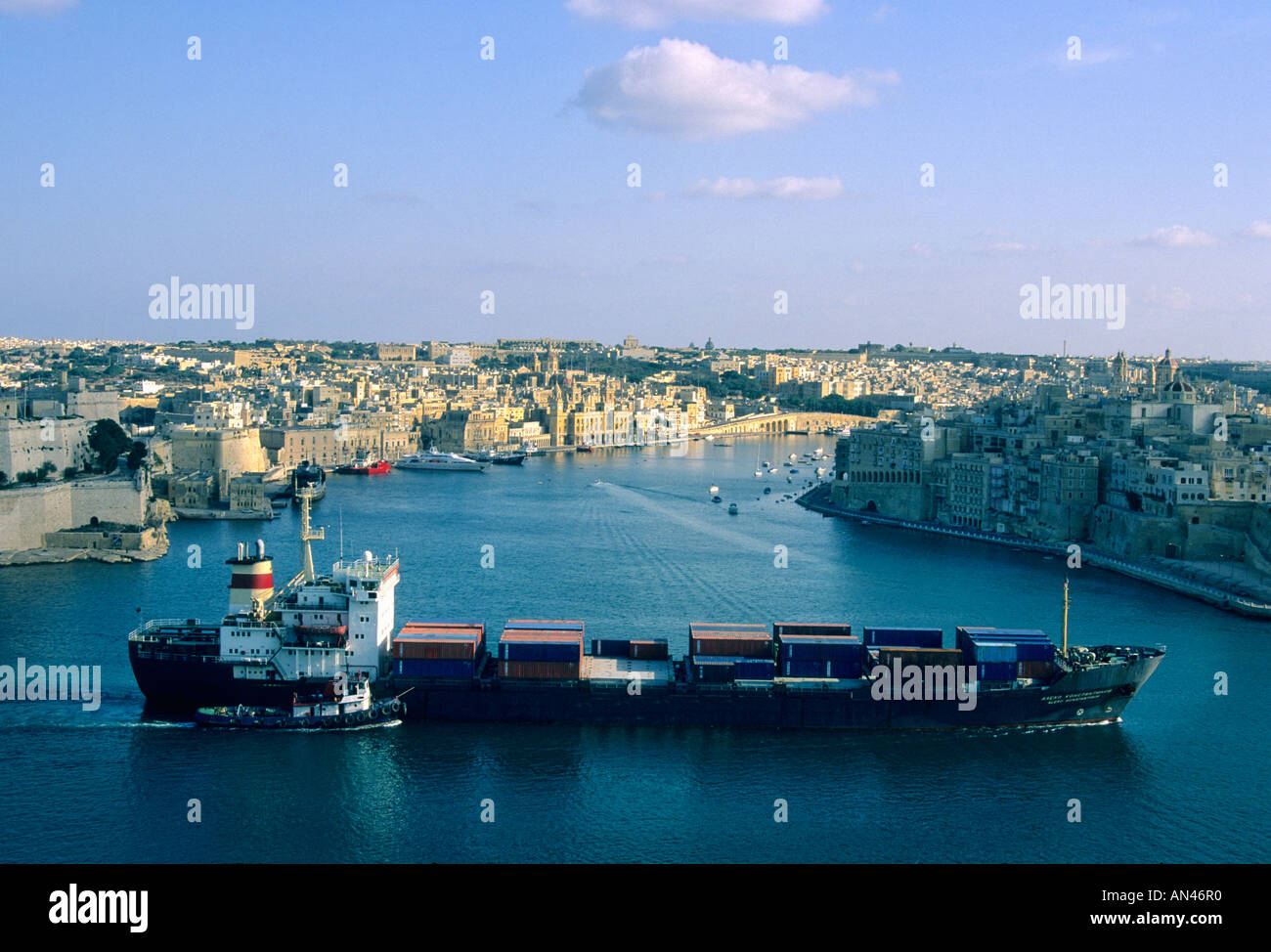Grand cargo qui navigue dans le port de La Valette, Malte / port - avec un bateau-pilote / remorqueur dans la lumière du midi Banque D'Images