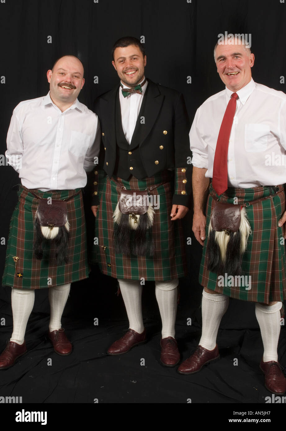 Sourire trois hommes portant le kilt en tartan gallois en face de toile noire, Pays de Galles, Royaume-Uni Banque D'Images