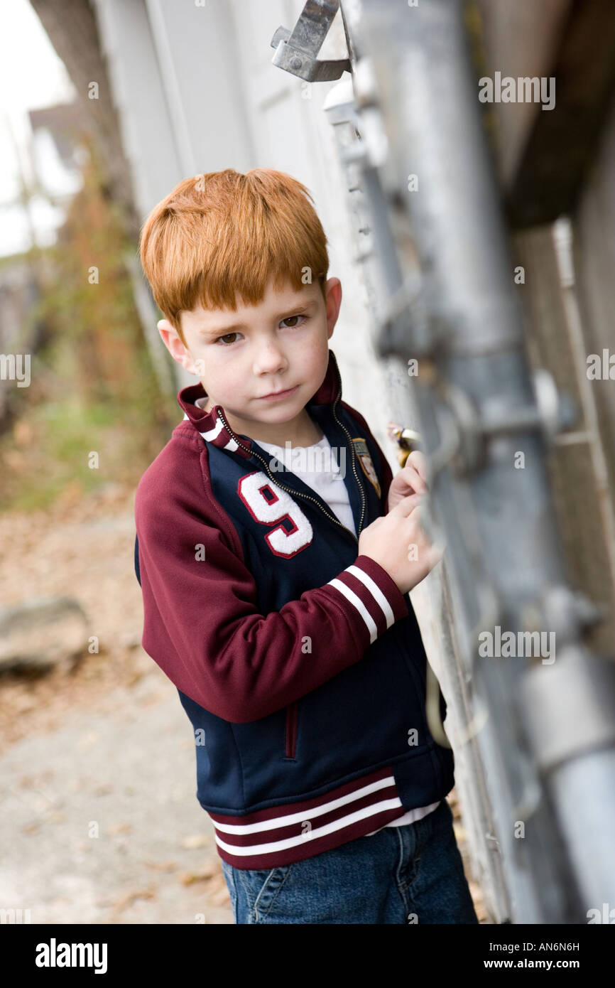 Tête rouge jeune garçon appuyé contre une clôture à la peur ou de la colère dans la ruelle. Banque D'Images