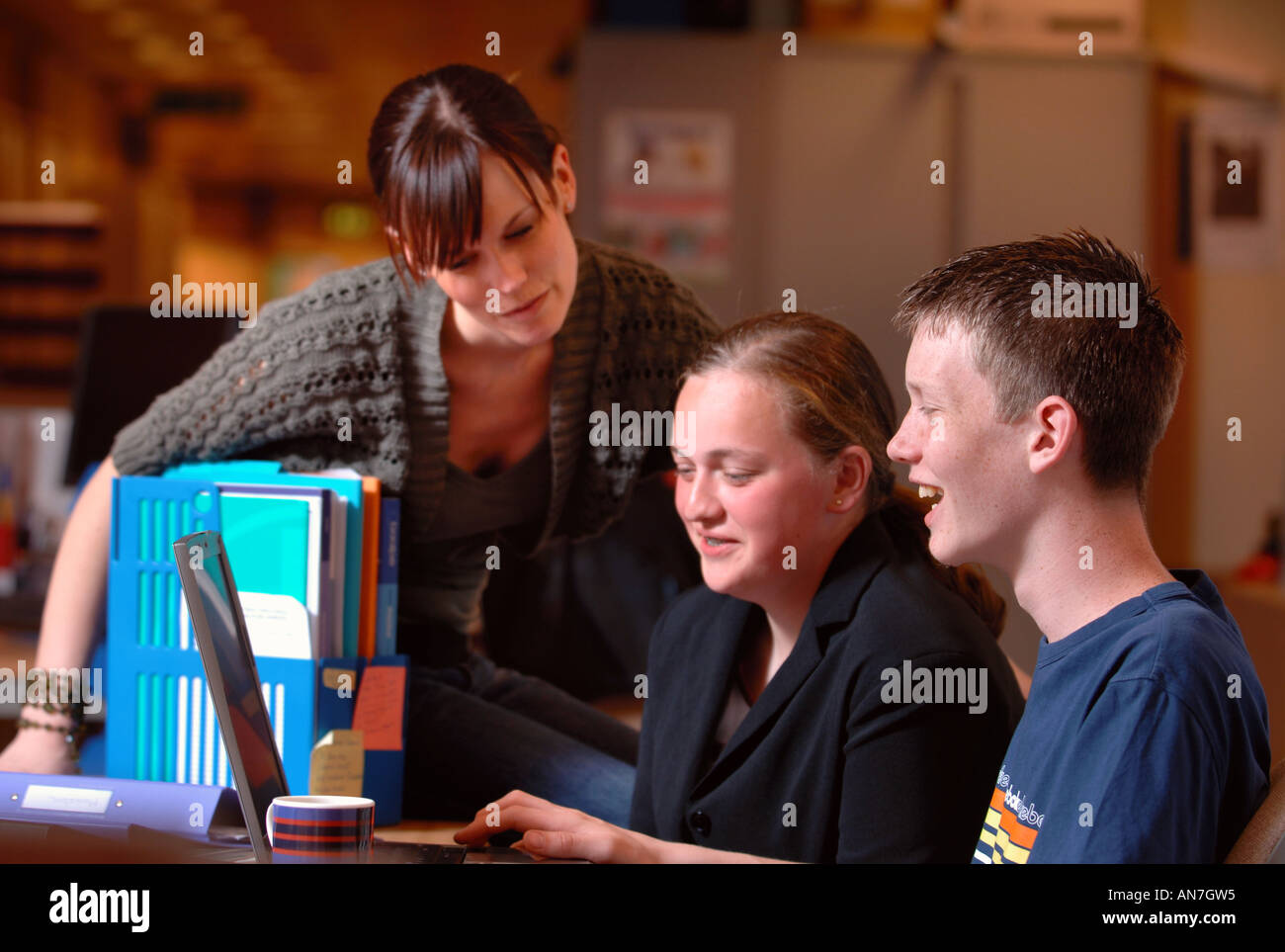 Une jeune fille et garçon TRAVAILLANT SUR UN ORDINATEUR PORTABLE EN COURS D'INSTRUCTION D'UN PROFESSEUR UK Banque D'Images