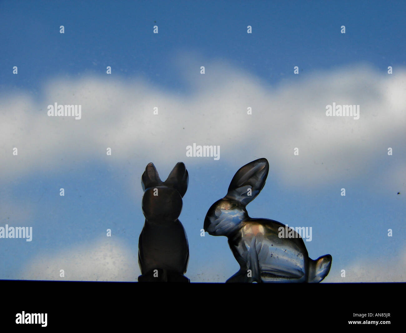 Deux lapins cristal contre une vitre avec des nuages derrière Banque D'Images