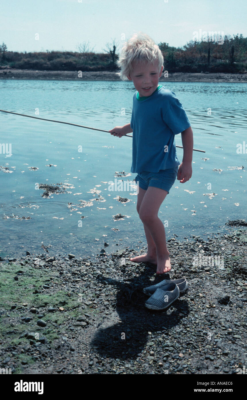 Petit garçon blond en short bleu et tee shirt prétendant à pêcher dans un  lac Photo Stock - Alamy