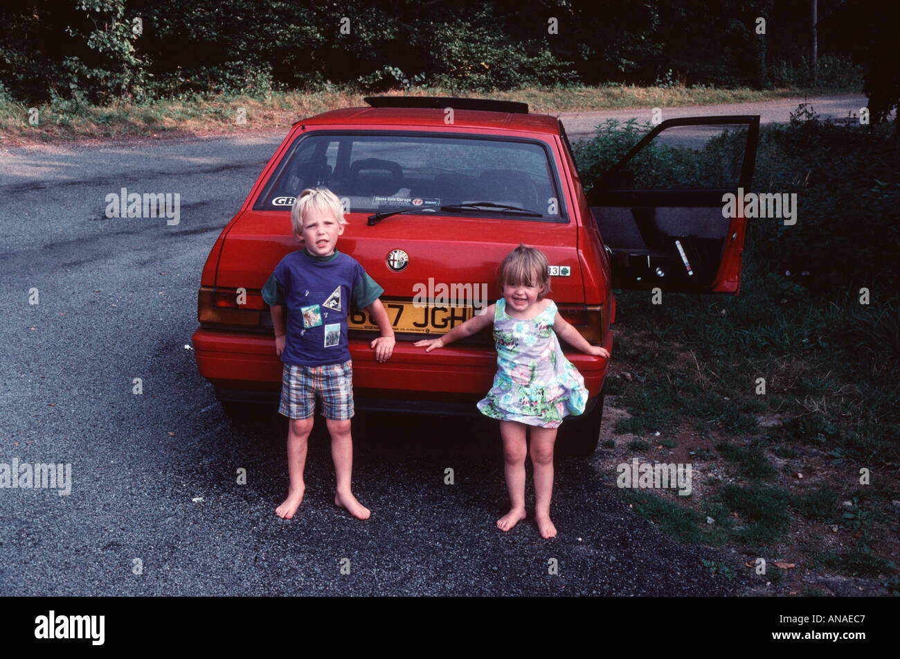 Deux petits enfants un garçon et une fille s'appuyer contre une voiture Alfa  Romeo rouge avec happy holiday smiles Photo Stock - Alamy