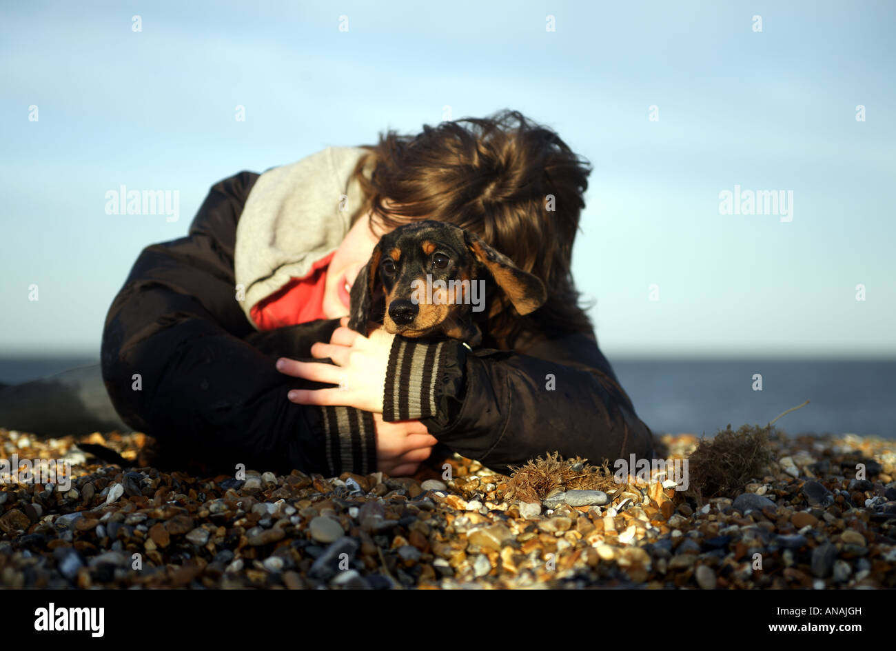 Jeune garçon embrasse son chiot sur une plage au soleil Banque D'Images