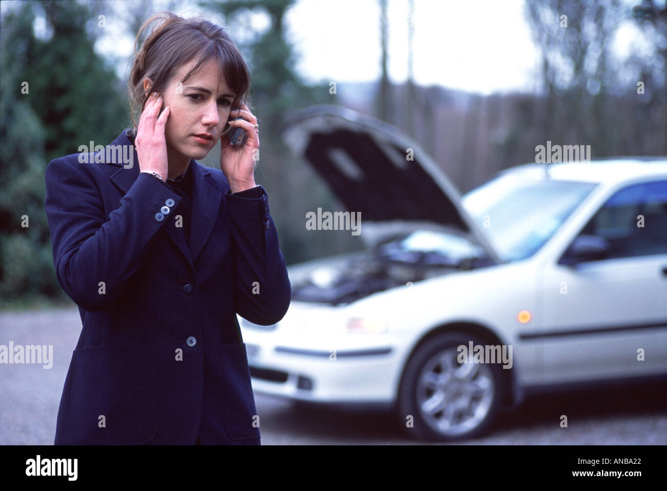 Young Woman talking on a cell phone with a broken down car dans l'arrière-plan Banque D'Images