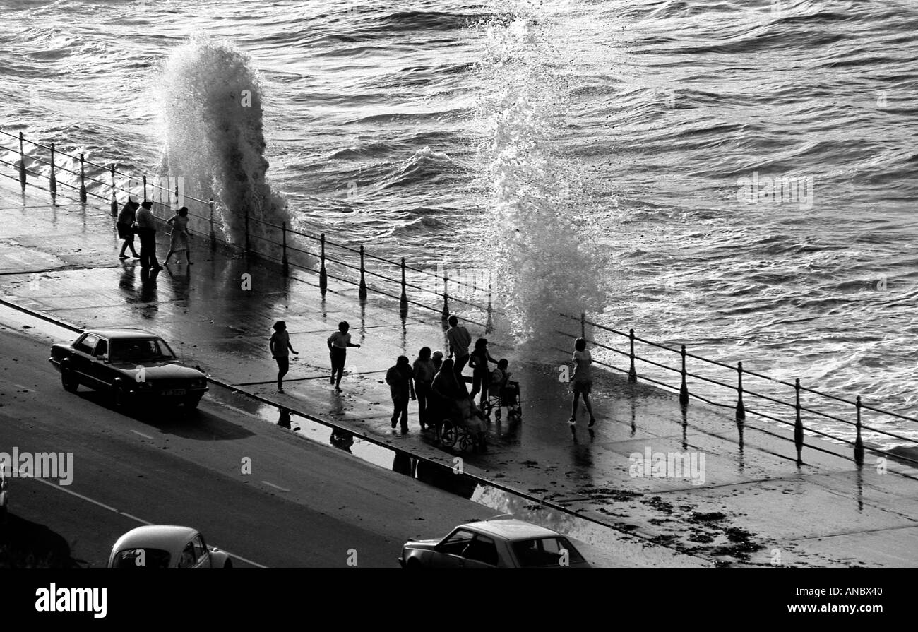 Éclaboussures des vagues sur le front de mer avec des gens en silhouette à Scarborough North Yorkshire Banque D'Images