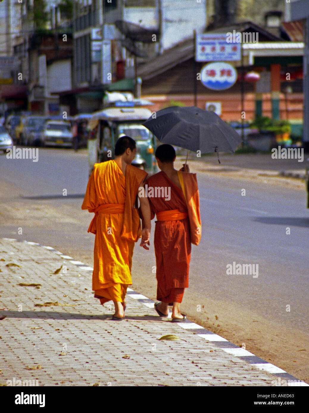 Paire de novices en vêtements colorés marcher dans les rues du centre-ville de Luang Prabang parapluie sous ombrage Laos Asie du sud-est Banque D'Images