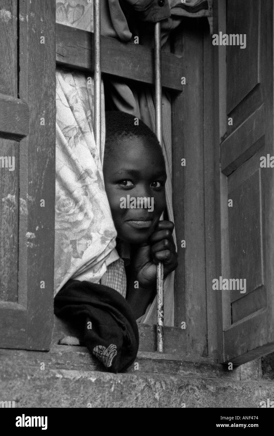 Enfant souriant du bidonville d'Acholy quart à la fenêtre de sa cabane en bois Kampala Ouganda Afrique de l'Est Banque D'Images