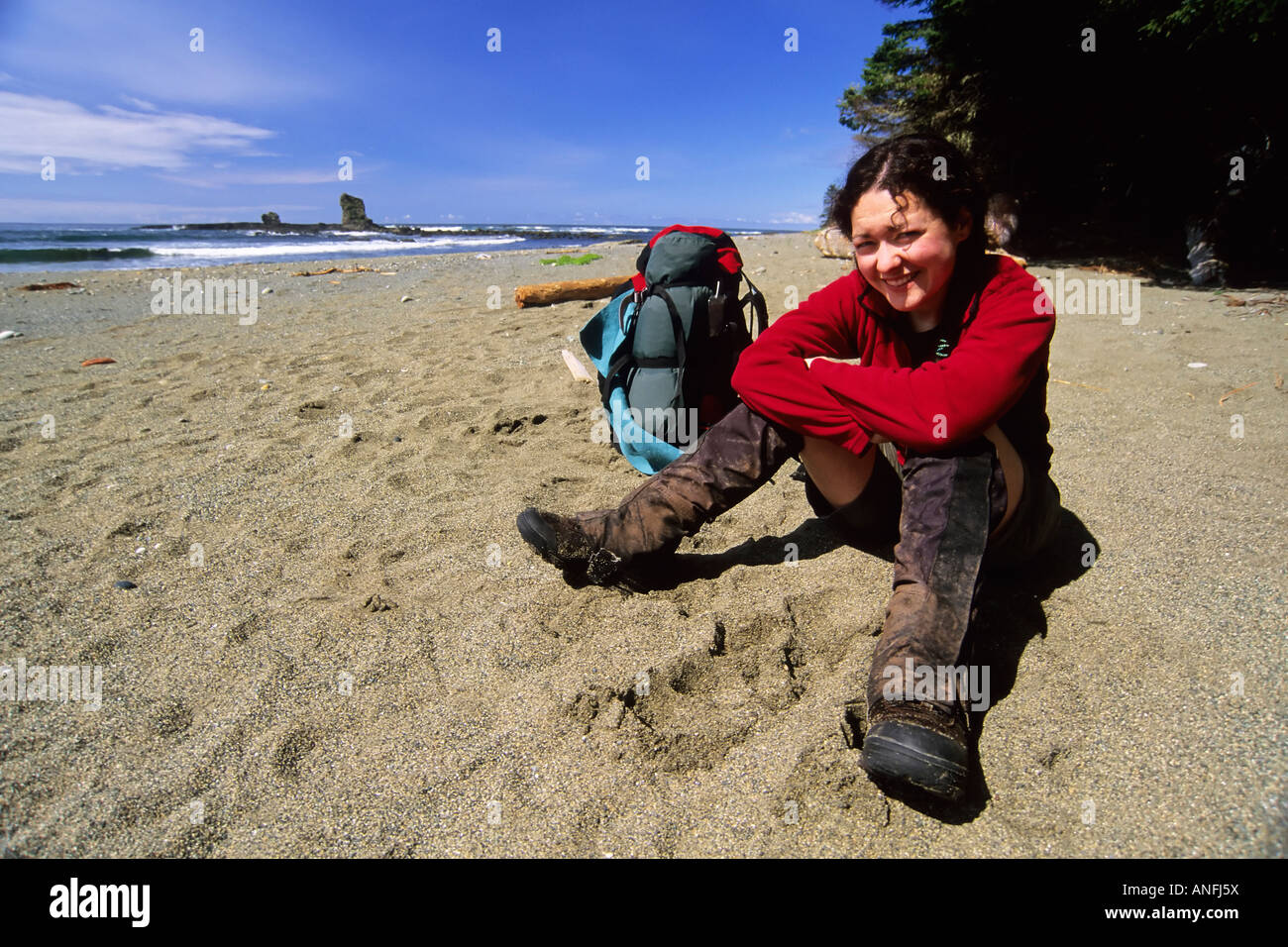 Une jeune femme (20-25) prend une pause de la randonnée le long d'une section de plage de la côte ouest sentier près du ruisseau Carmanah Pacific Rim en Banque D'Images