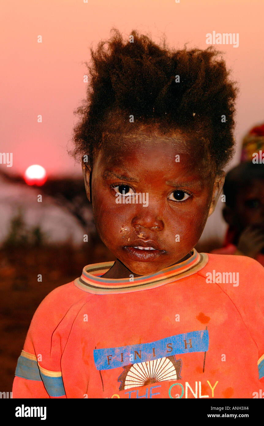 Une jeune fille sale, de l'Angola semble malheureusement à l'appareil photo alors que le soleil se couche derrière elle Banque D'Images