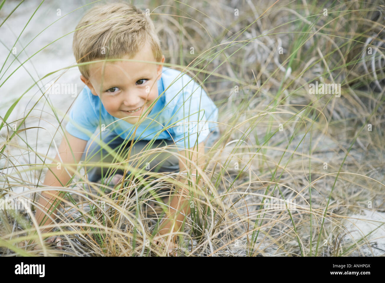 Jeune garçon accroupi dans l'herbe haute, à l'écart, smiling Banque D'Images