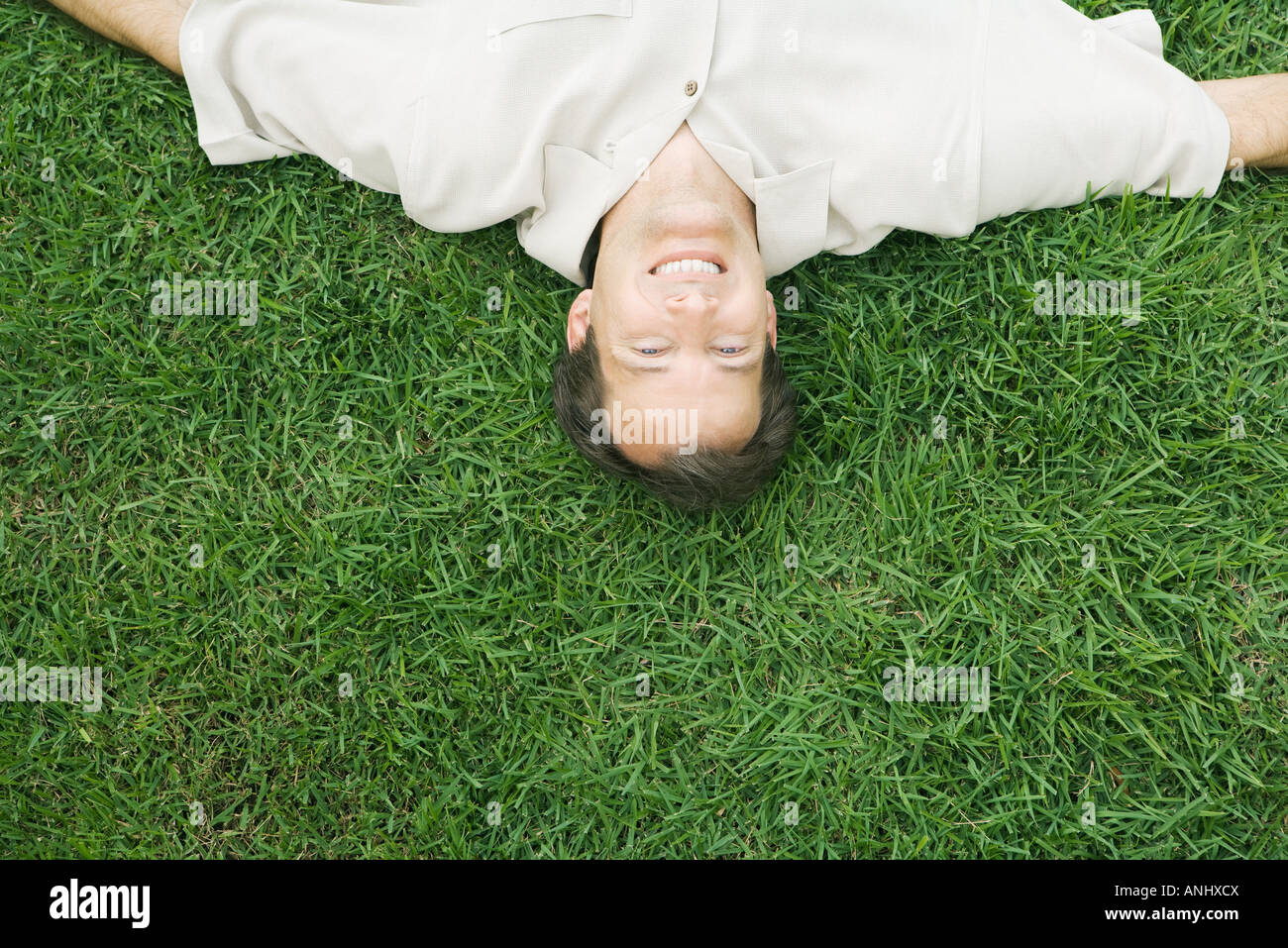 Homme couché à l'envers dans l'herbe, smiling at camera, portrait high angle view Banque D'Images
