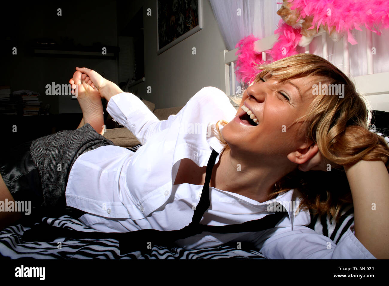 Femme riant joyeusement tout en étant allongée sur un couvre-lit à motif zèbre, vêtue d'une chemise blanche et d'une cravate noire, dans une pièce lumineuse et confortable. Banque D'Images