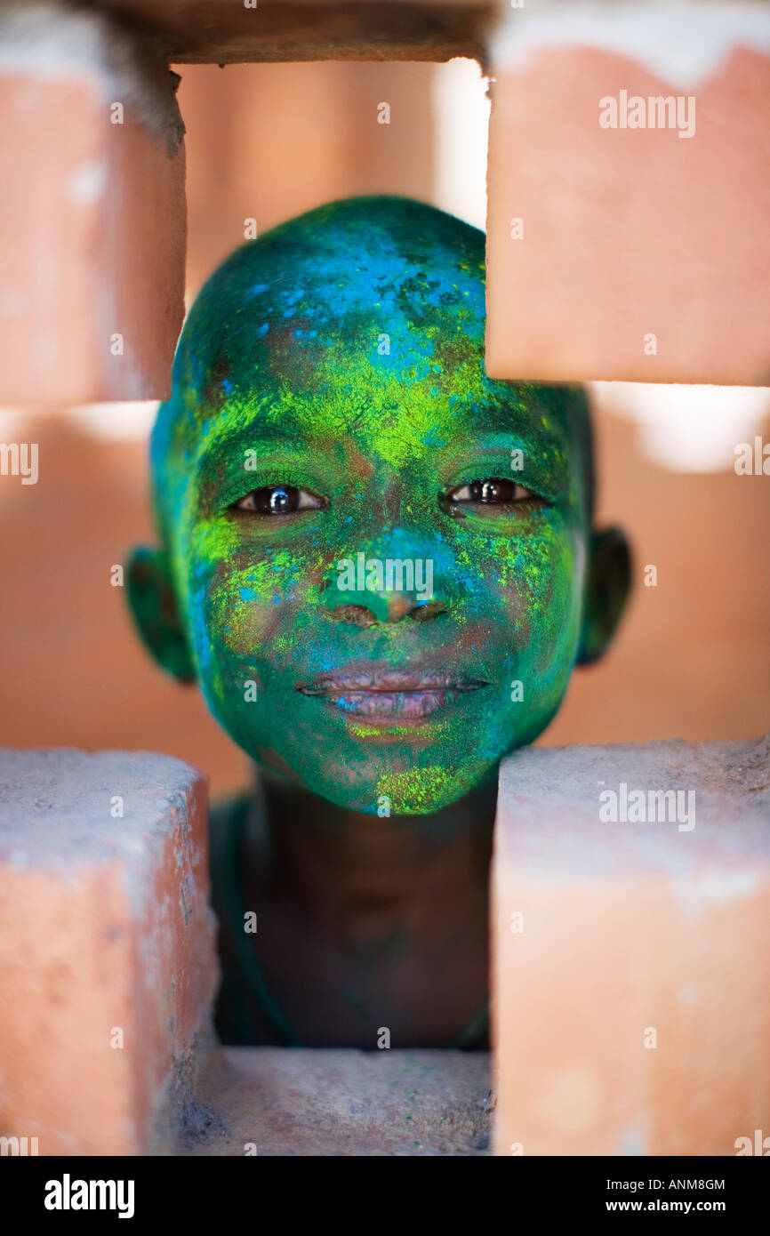 Jeune Indien garçon couvert de poudre de couleur pigment de regarder à travers un trou transversal dans un bâtiment en brique. L'Inde Banque D'Images