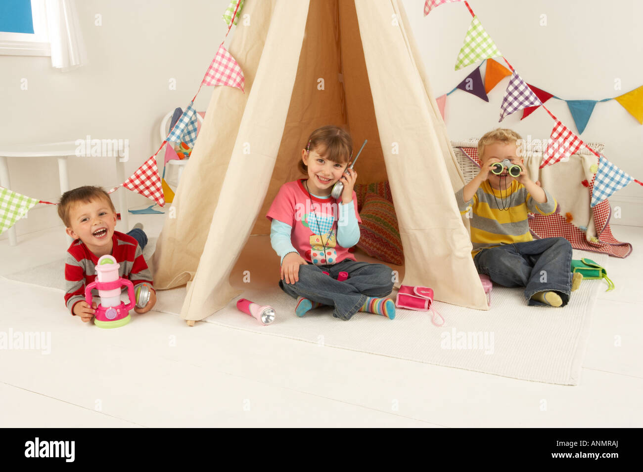 Trois enfants jouer dans un scénario de camping avec une tente décorée dans bunting, jumelles et d'une lanterne Banque D'Images