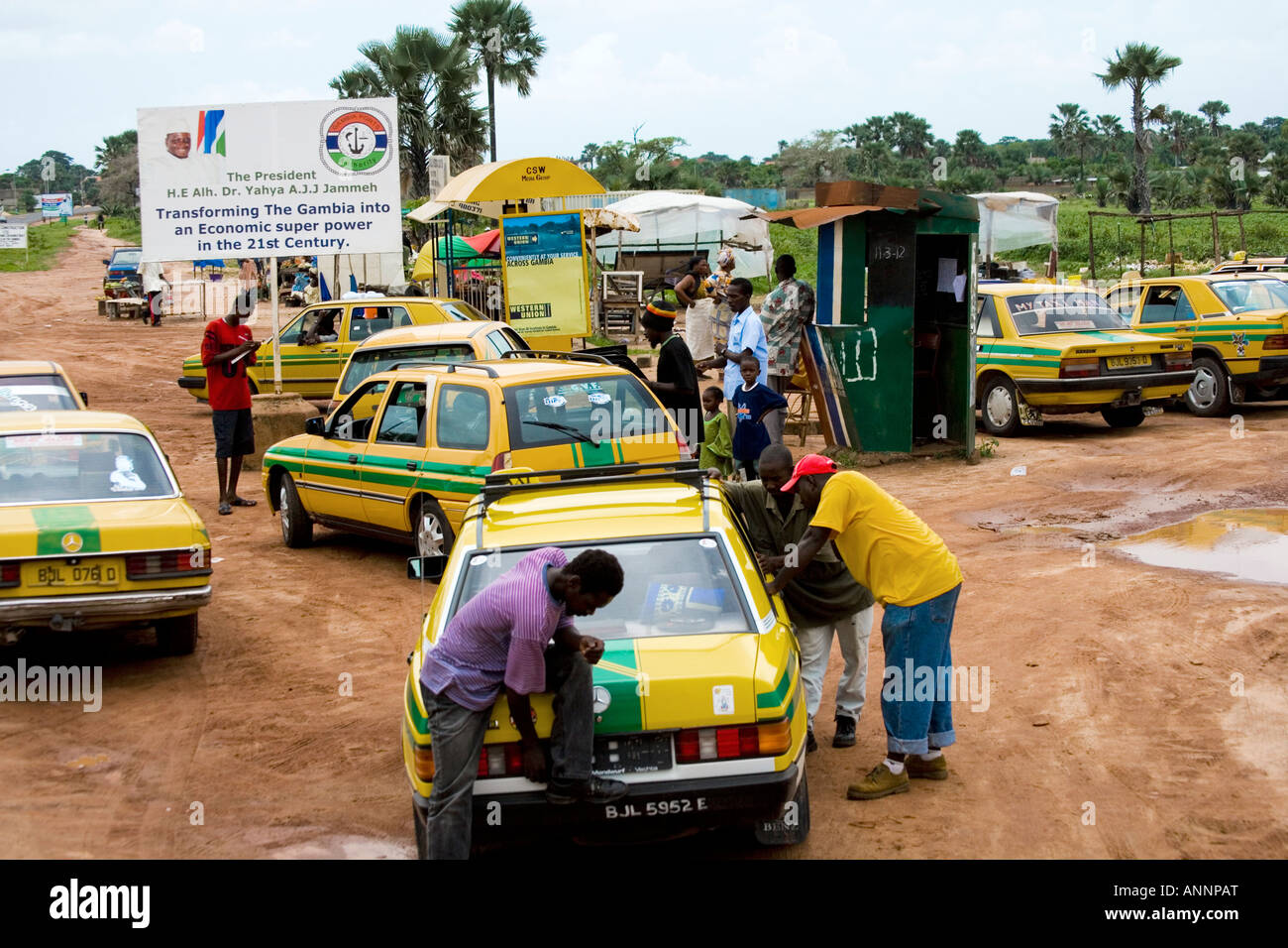 Station de taxi par la route en Gambie avec affiche de propagande sur le Président Yahya AJJ Jammeh en arrière-plan. Banque D'Images
