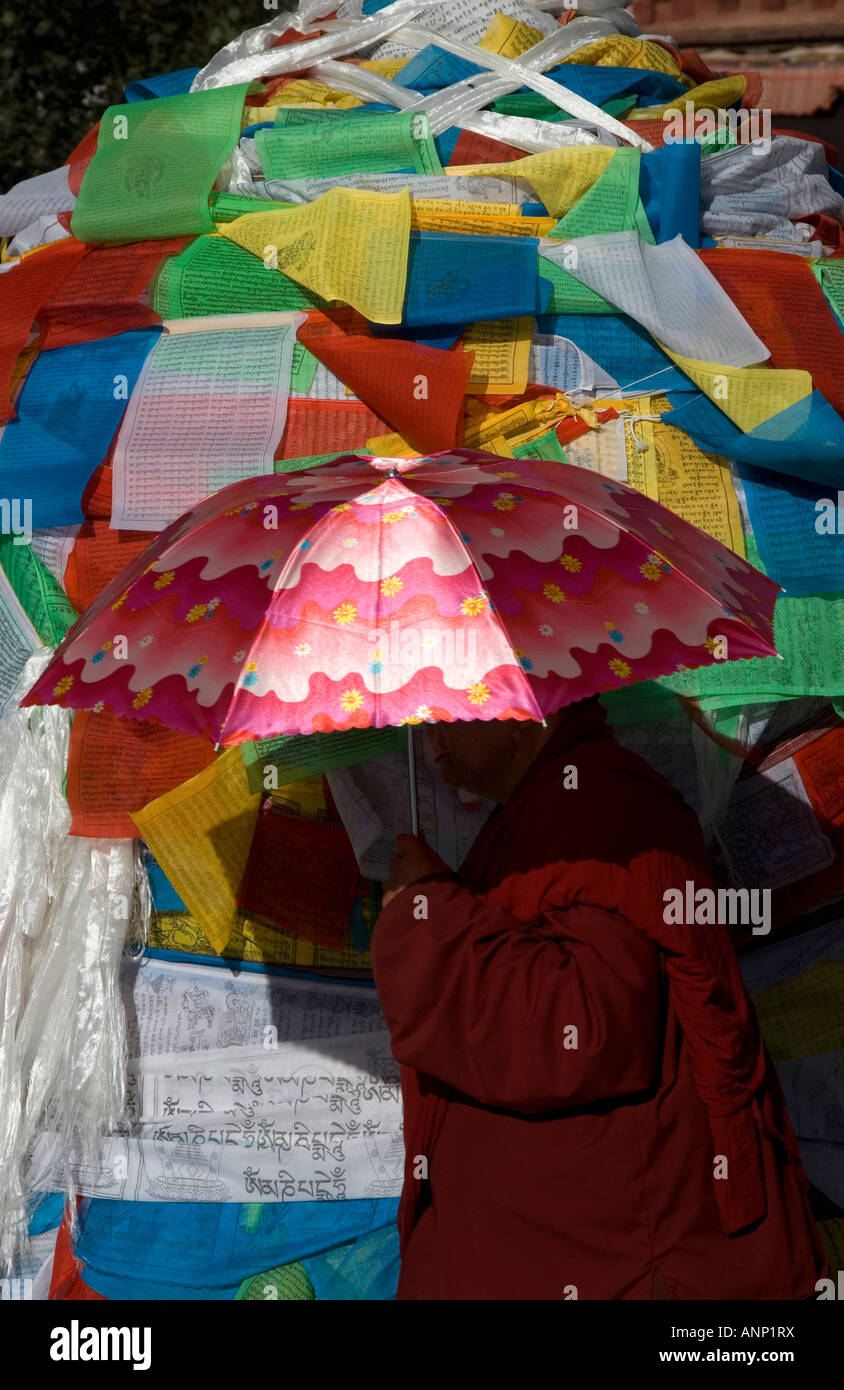 Un moine se protéger du soleil direct comme il passe un post enveloppés dans des drapeaux de prière. Banque D'Images