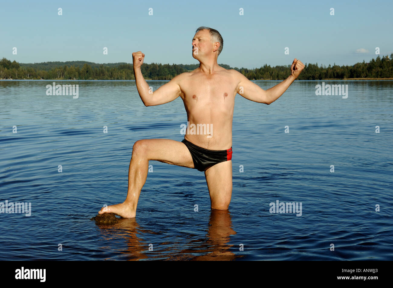 L'homme se tient dans l'eau et fléchit ses muscles, lac Kirchsee, Haute-Bavière, Allemagne Banque D'Images
