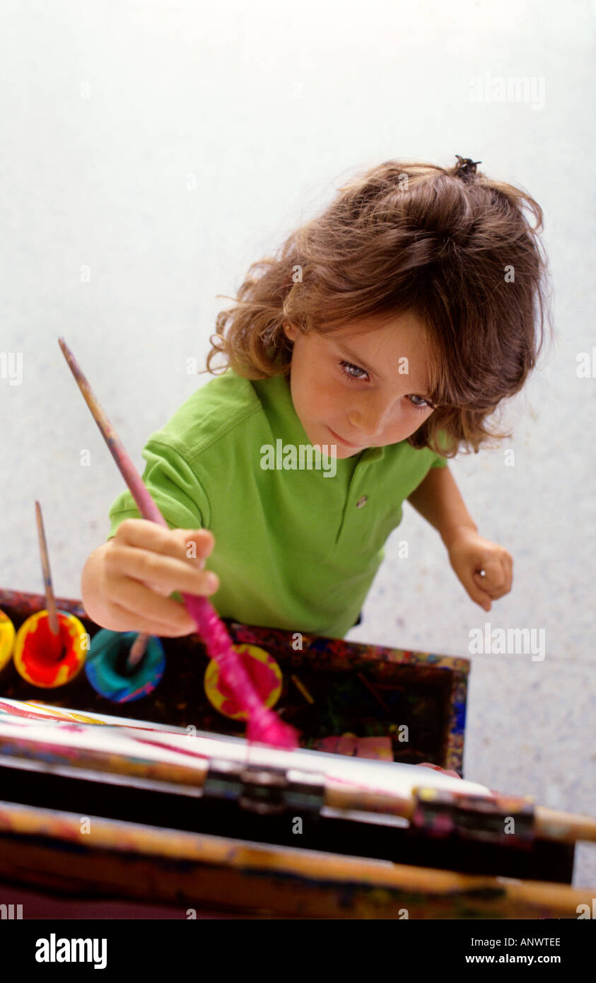 CLASSE D'ART Infant Girl 4 à 5 ans avec pinceau se concentre sur ses œuvres d'art de peinture au chevalet d'école en bois traditionnel dans la salle de classe d'art. Banque D'Images