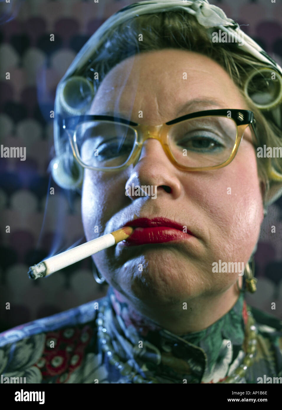 Femme avec friser sur sa tête et lunettes fumer une cigarette Banque D'Images