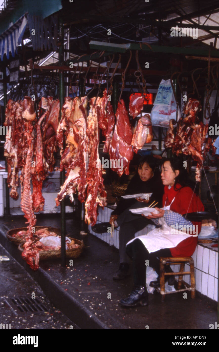 Deux femme de la région de manger le déjeuner à côté de la carcasse à la vente à leur échoppe de marché,Chengdu, Sichuan Province, China. Banque D'Images
