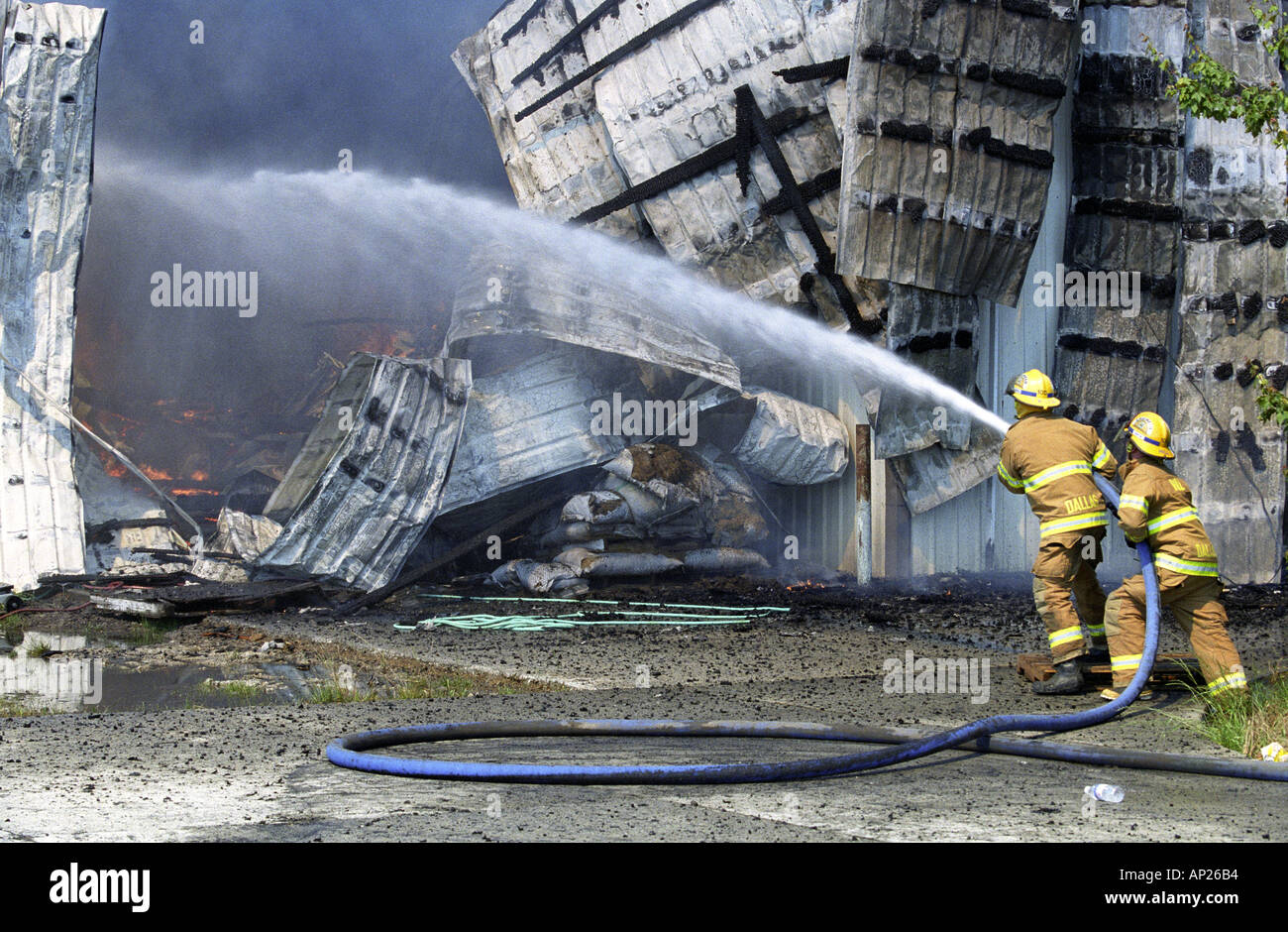 Deux pompiers tenir un flexible pulvériser de l'eau sur une tôle buring barn Banque D'Images