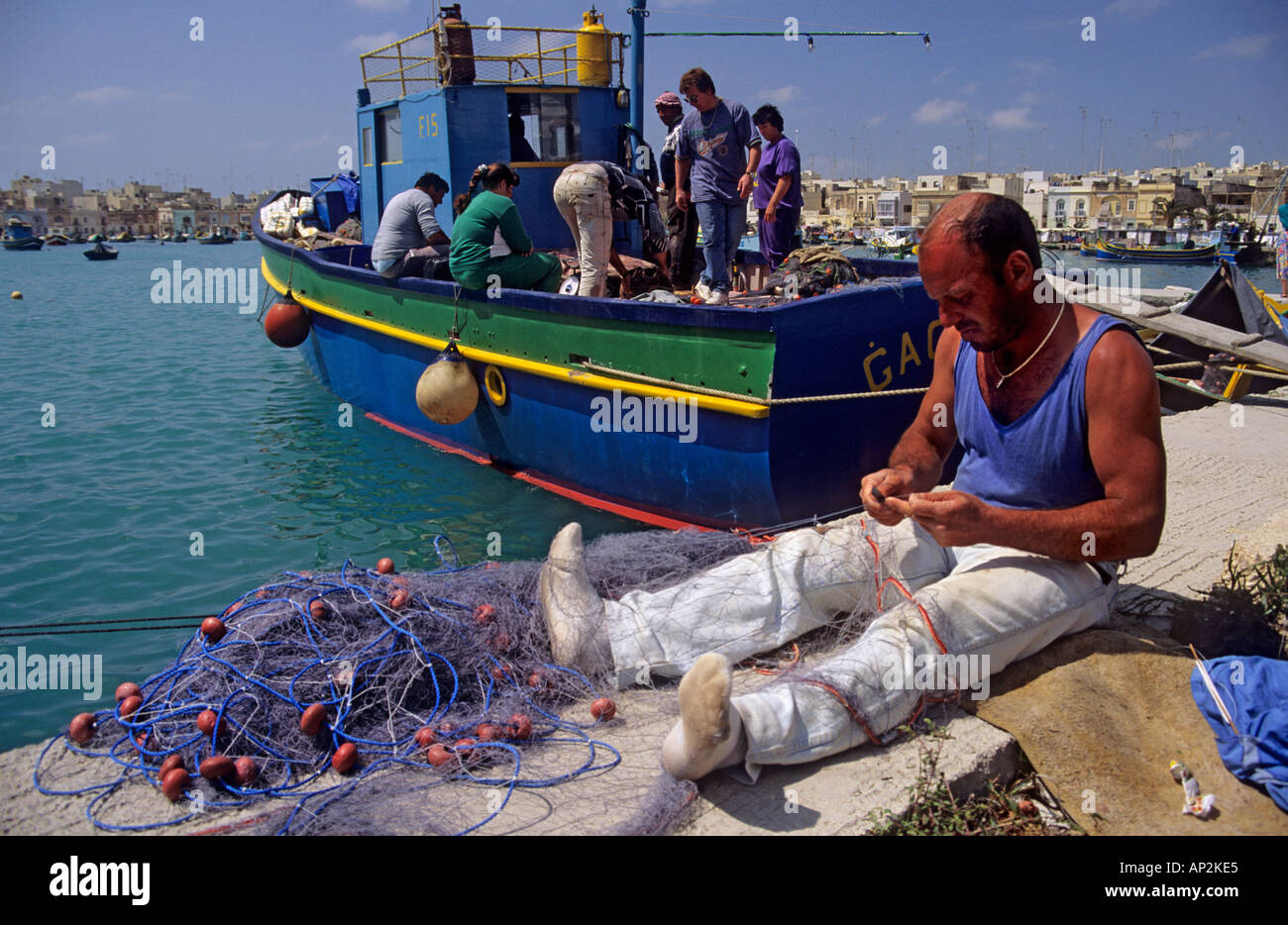 Fisherman mending moustiquaires avec des bateaux dans le port de Malte Europe Banque D'Images