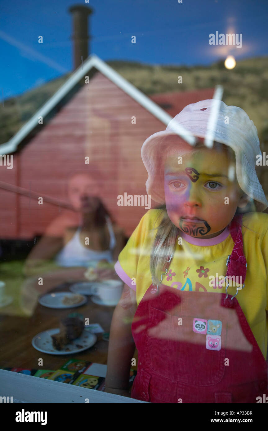 Fille avec facepainting (comme un moko maori, Tatoo), vue depuis une fenêtre, célébrations à Waitangi Day, Okains Bay sur la péninsule de banque Banque D'Images