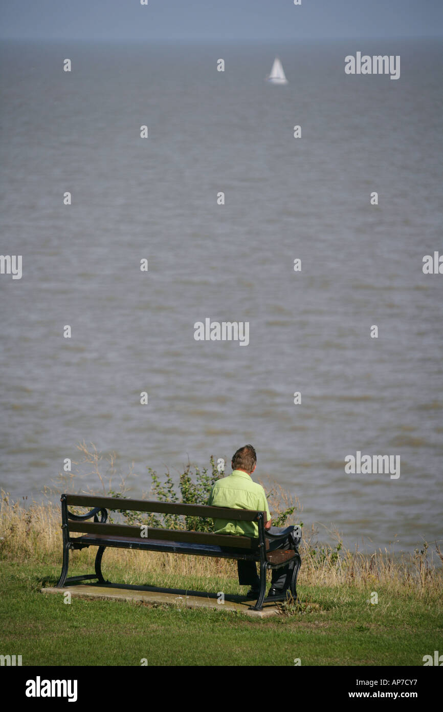 L'homme assis sur un banc sur le front, Frinton and-on-Sea, Essex, Angleterre, Royaume-Uni. Banque D'Images