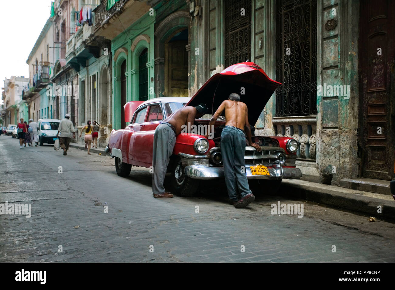 Voiture américaine classique se trouve stationné à l'extérieur des bâtiments anciens à La Havane (Cuba) avec deux hommes la réparation du moteur. Banque D'Images