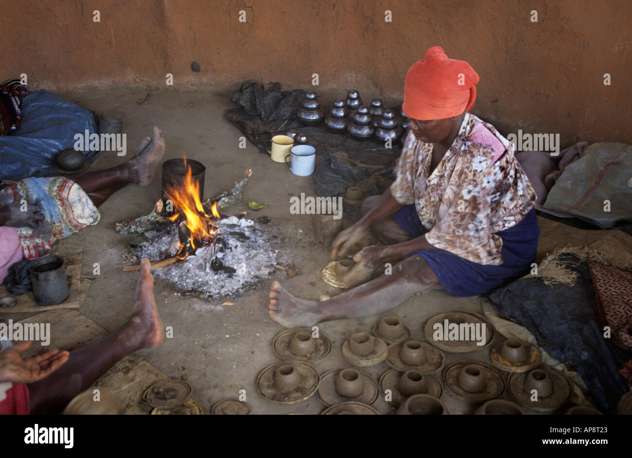 Femme africaine dans une hutte de boue rendant les pots d'argile à côté d'un feu ouvert Afrique Zimbabwe Banque D'Images