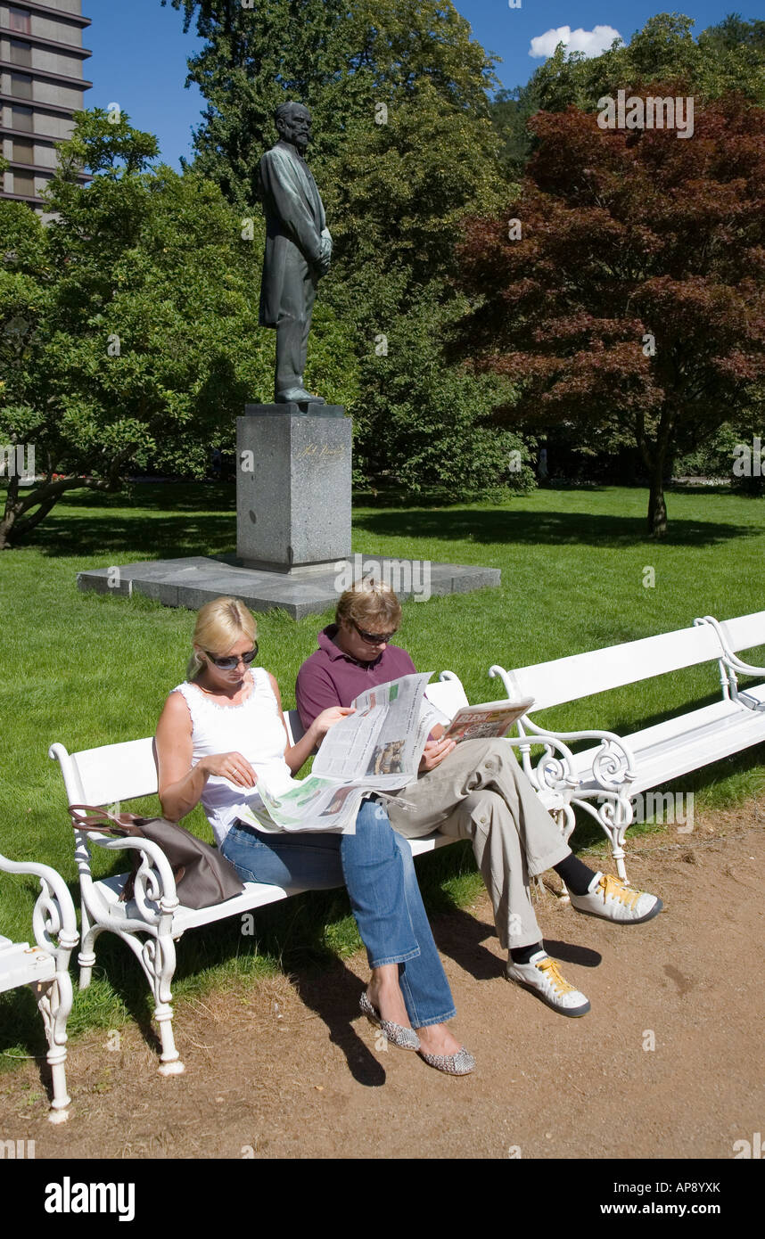 Deux personnes de lire les journaux en parc avec statue de Dvorak derrière Karlovy Vary République Tchèque Banque D'Images