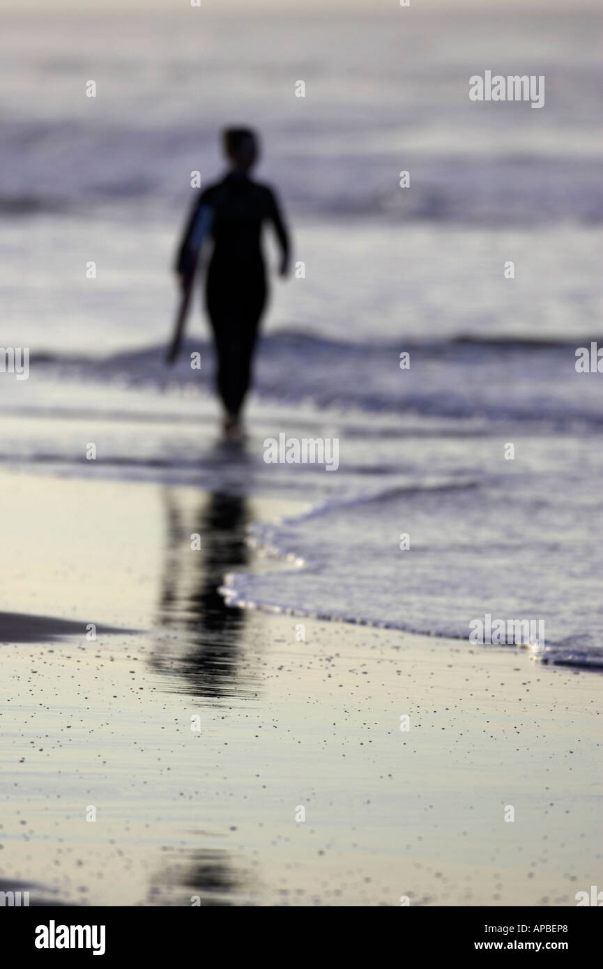 Hors focus silhouette de femme bodyboarder en portant son bodyboard dans la lumière du soir sur la plage de White Rocks Banque D'Images