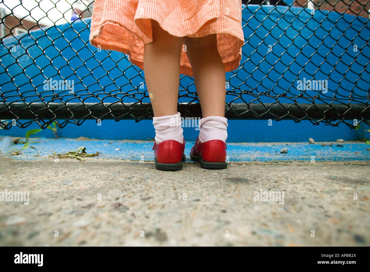 Jolie jambes de jeune fille avec des chaussures rouge et bleu robe à côté de clôture. Low angle bobby chaussettes Banque D'Images