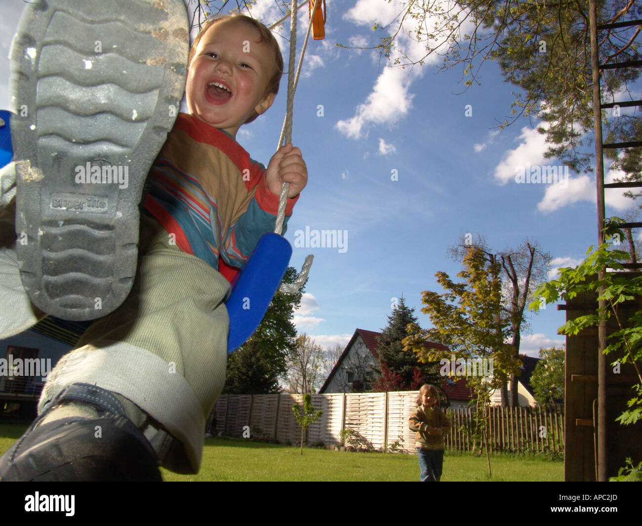 Garçon de deux ans sur un enfant balançoires jubilant swing sur l'arbre dans le jardin. Banque D'Images