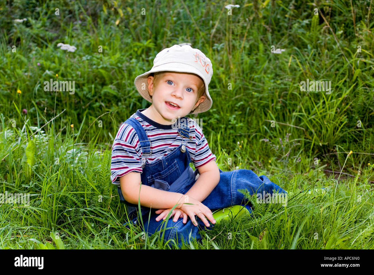 Un garçon de trois ans avec un slouch hat est assis dans l'herbe Banque D'Images