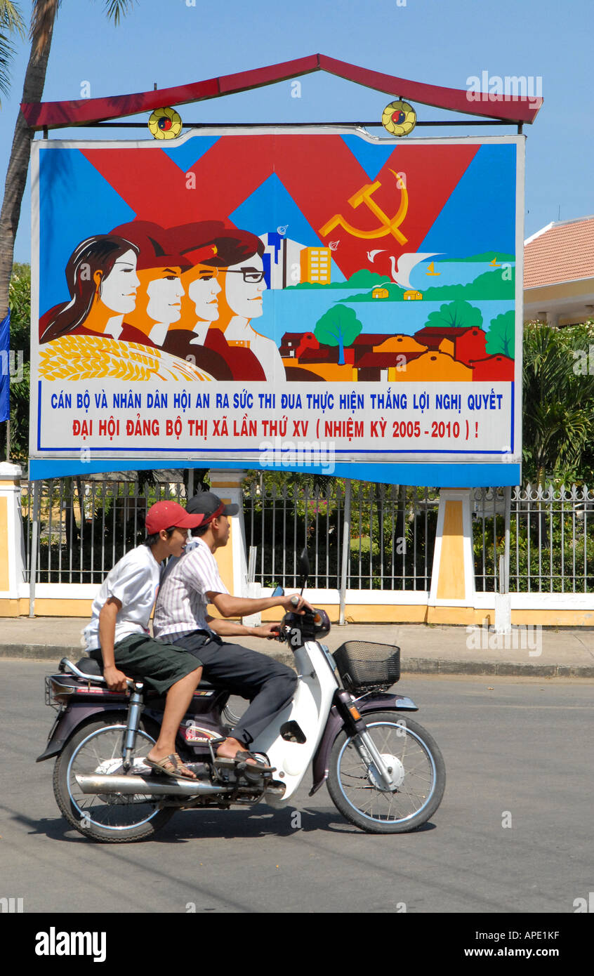 Moto passant devant une affiche socialiste dans la ville de Hoi An, Vietnam Banque D'Images