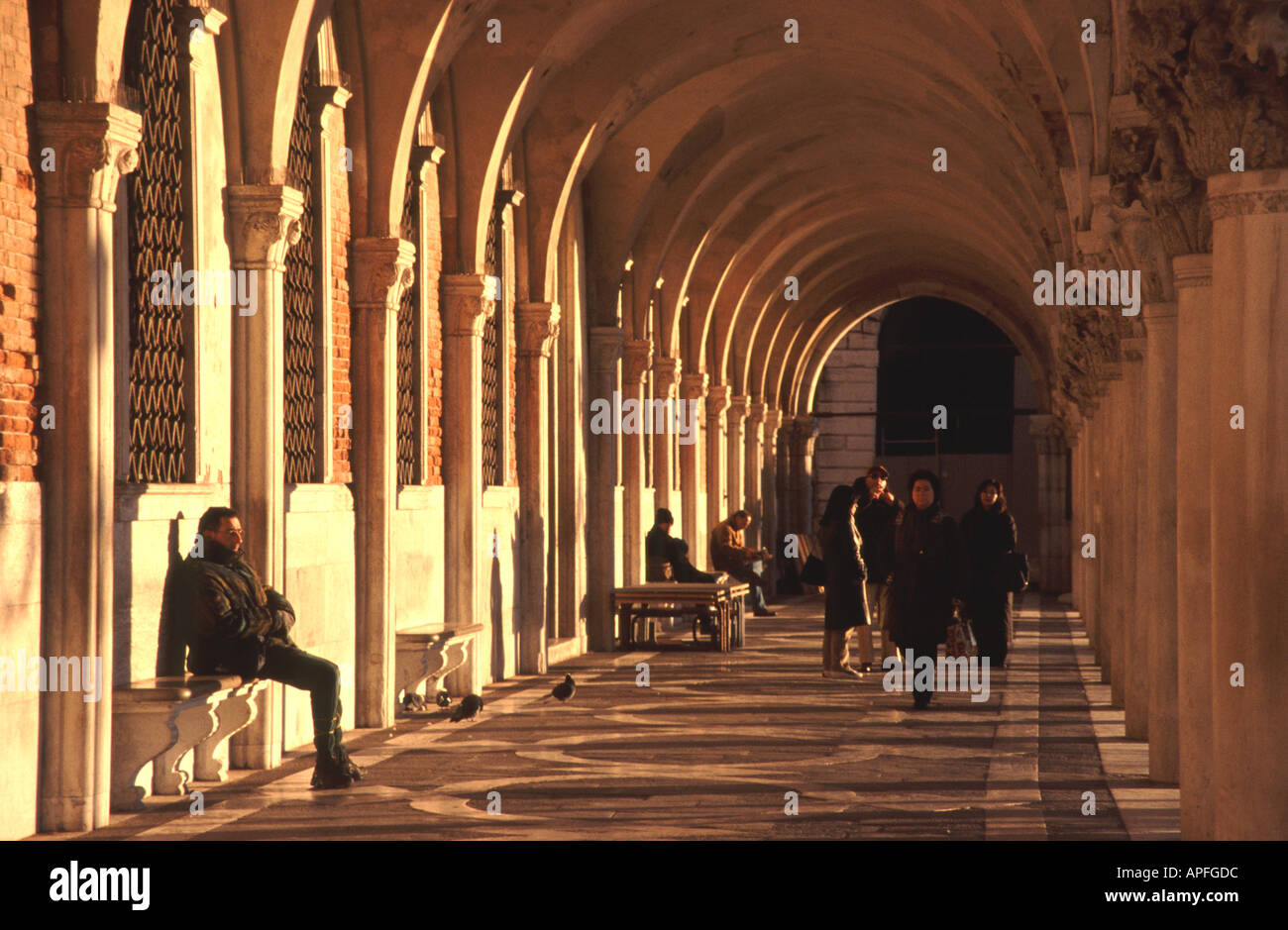 Venise, Italie. Les personnes bénéficiant de l'hiver soleil dans une colonnade par le Palazzo Ducale (Palais des Doges) sur la Place St Marc. Banque D'Images