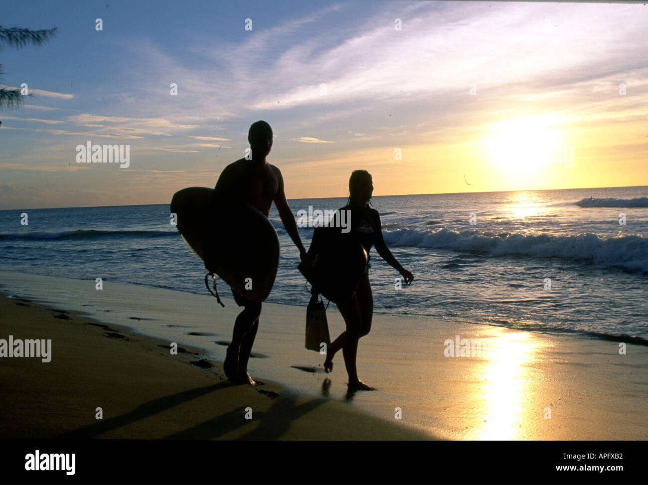 Couple en train de marcher sur la plage au coucher du soleil avec des planches Banque D'Images