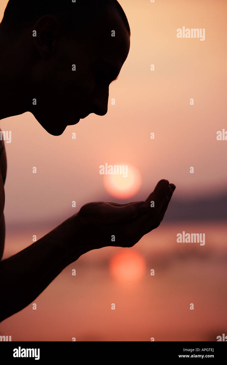 Silhouette d'un homme avec des creux des mains en dessous d'un coucher de soleil Banque D'Images