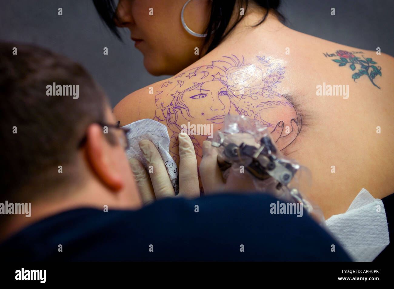 Un tatouage artiste au travail encrant un dessin sur l'épaule d'une femme. Photo de Jim Holden. Banque D'Images