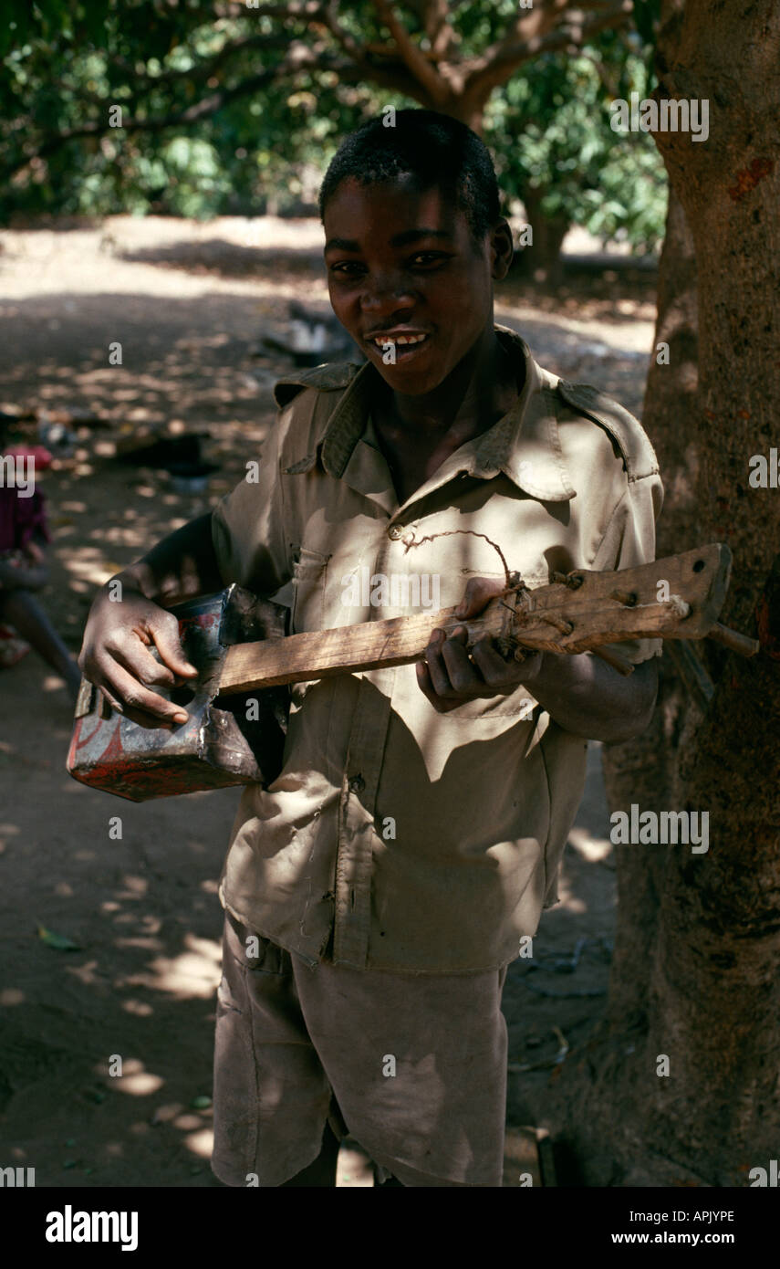 Garçon jouant une guitare faite maison à l'ombre d'un manguier, Fulaza village, par North Luangwa National Park, Zambie. Banque D'Images