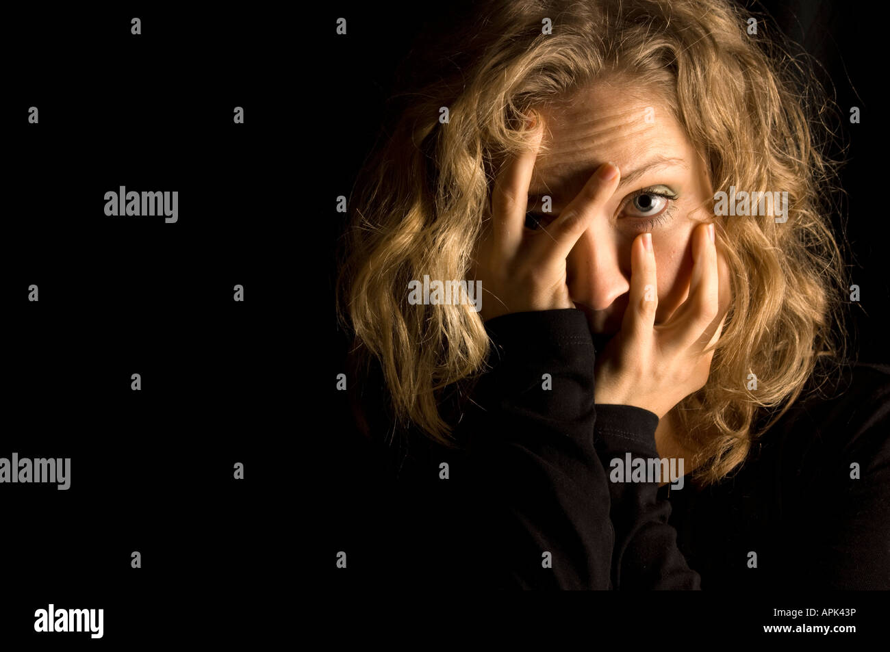 Jeune blond woman holding sa tête dans ses mains en studio contre fond noir se reflète entre ses doigts Banque D'Images
