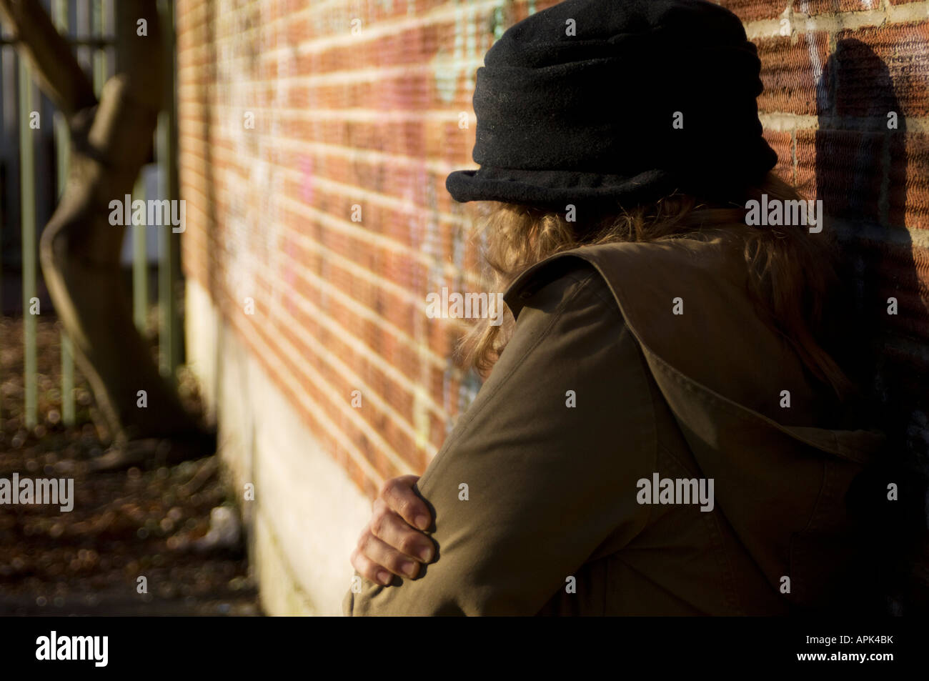 Vue arrière du jeune femme seule, près de mur de briques couverts de graffitis ramassées dans son manteau à la triste déprimé vulnérables solitaire Banque D'Images
