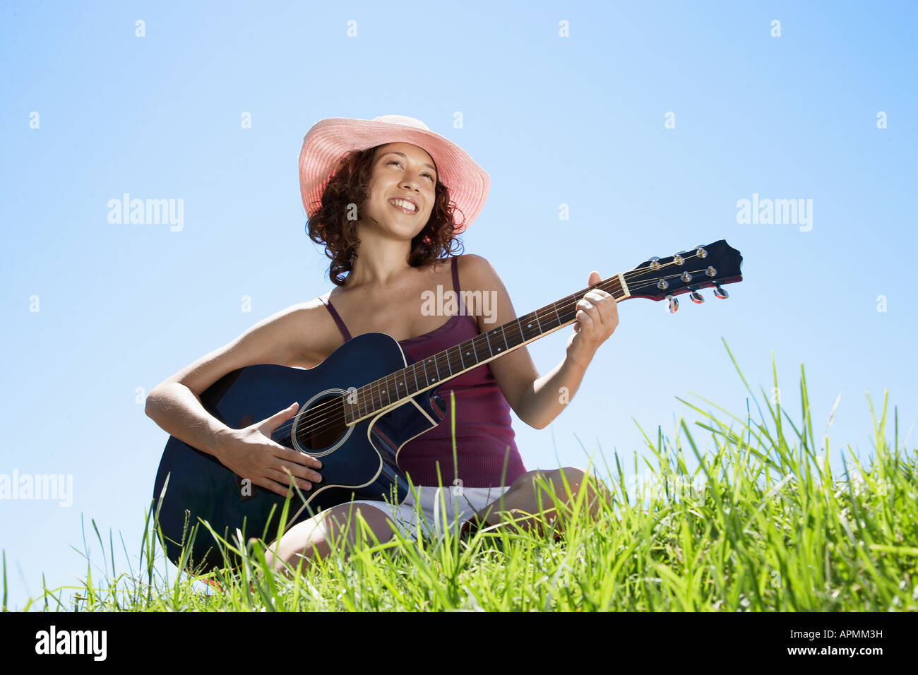 Jeune femme jouant de la guitare sur l'herbe (low angle view) Banque D'Images