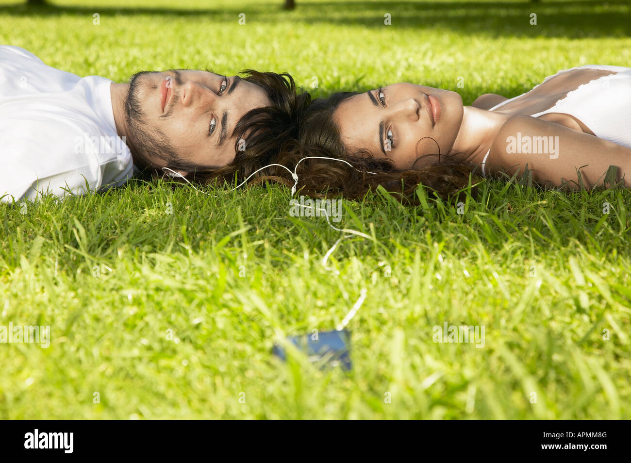 Jeune couple partageant un lecteur MP3 sur l'herbe Banque D'Images