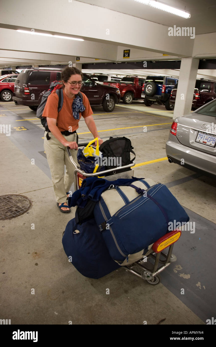 Woman poussant chariot aéroport laden avec des sacs par location de voitures parking gratuit salon Vancouver Canada Banque D'Images