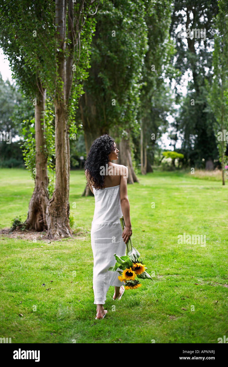 Jeune femme avec des tournesols Walking in Garden Banque D'Images