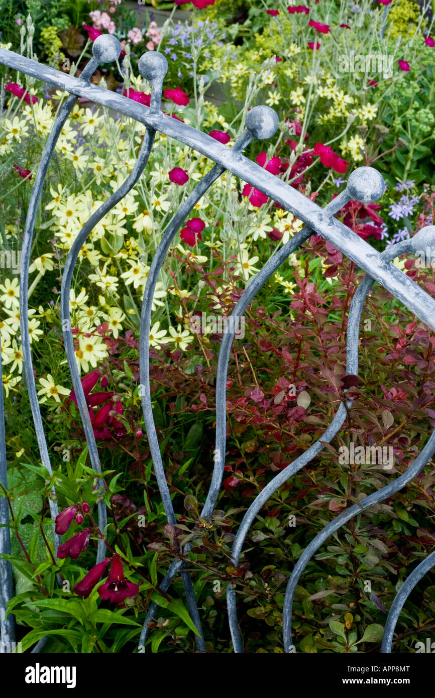 Garde-corps en ferronnerie décorative gris argent sur le bord du petit jardin avec rouge, rose et jaune fleurs derrière Banque D'Images